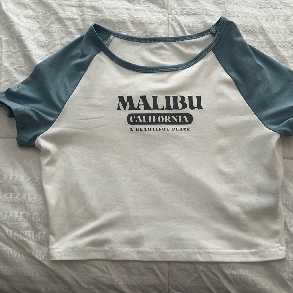 A white baby tee with blue raglan sleeves and a Malibu California print, photographed flat